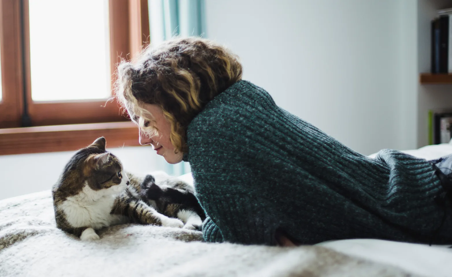 A woman and a cat looking at each other on a bed